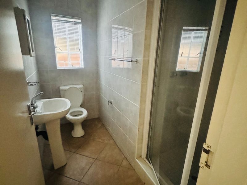 A functional bathroom featuring a pedestal basin, toilet, and a shower enclosure with tiled walls and flooring.