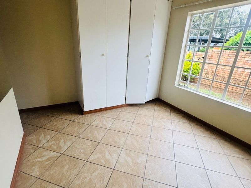 An empty bedroom featuring tiled flooring, built-in cupboards, and a large grid-pattern window providing natural light.