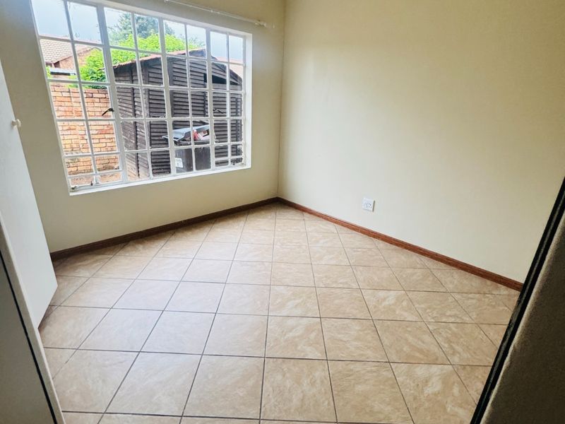 An empty bedroom featuring neutral tiled flooring, coving, and a large grid-pattern window providing natural light.