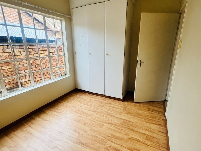 An empty bedroom featuring laminate flooring, a built-in wardrobe, and a large grid-pattern window providing natural light.
