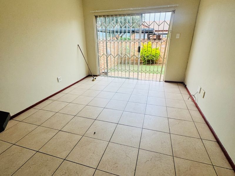 An empty living room featuring neutral tiled flooring and a sliding glass door with a security gate leading to the rear exterior.