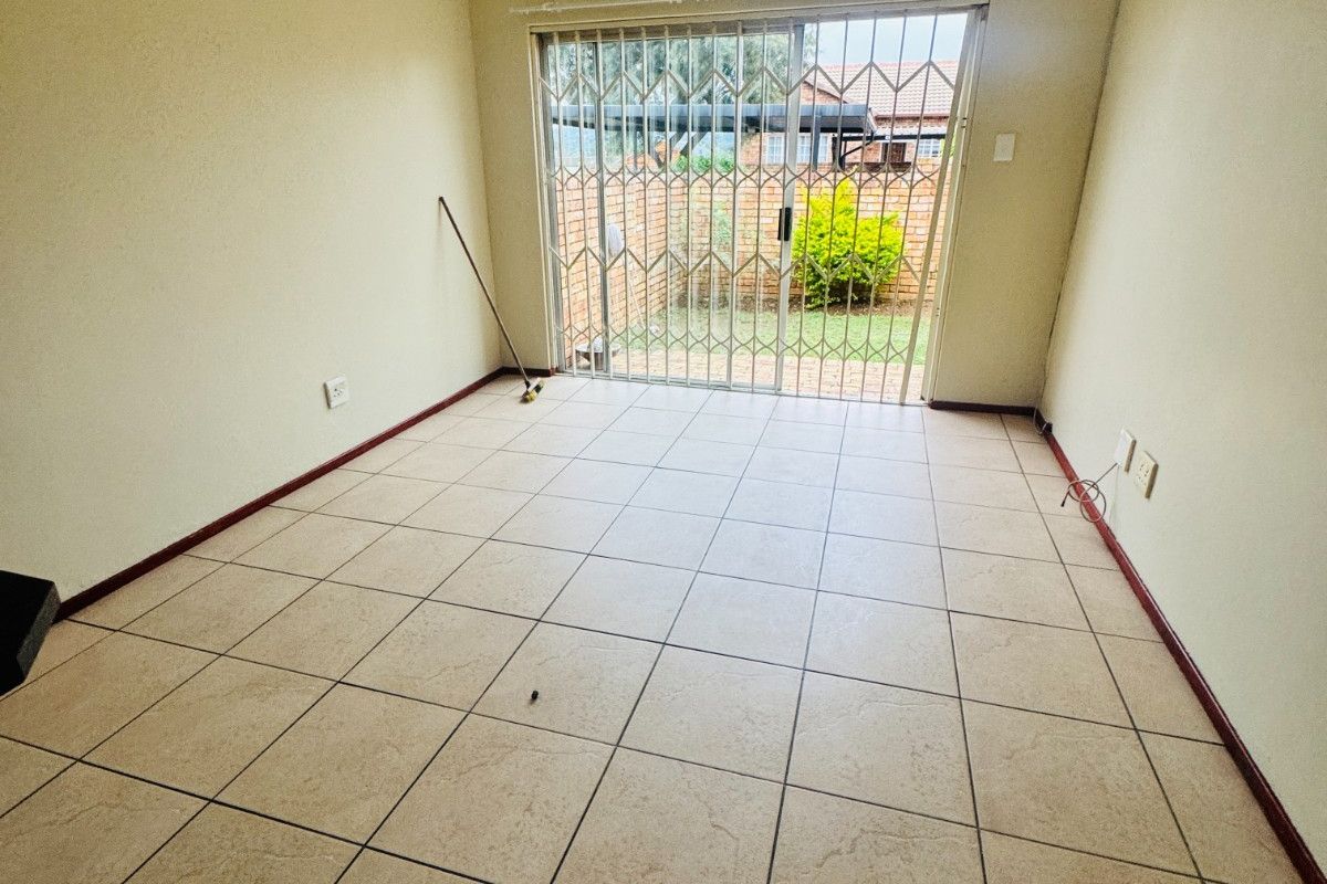 An empty living room featuring neutral tiled flooring and a sliding glass door with a security gate leading to the rear exterior.
