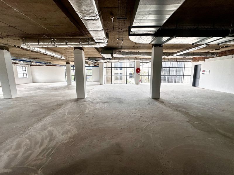 Spacious open-plan office shell featuring exposed concrete ceilings, industrial ducting, and large windows providing ample natural light, ready for custom fit-out.