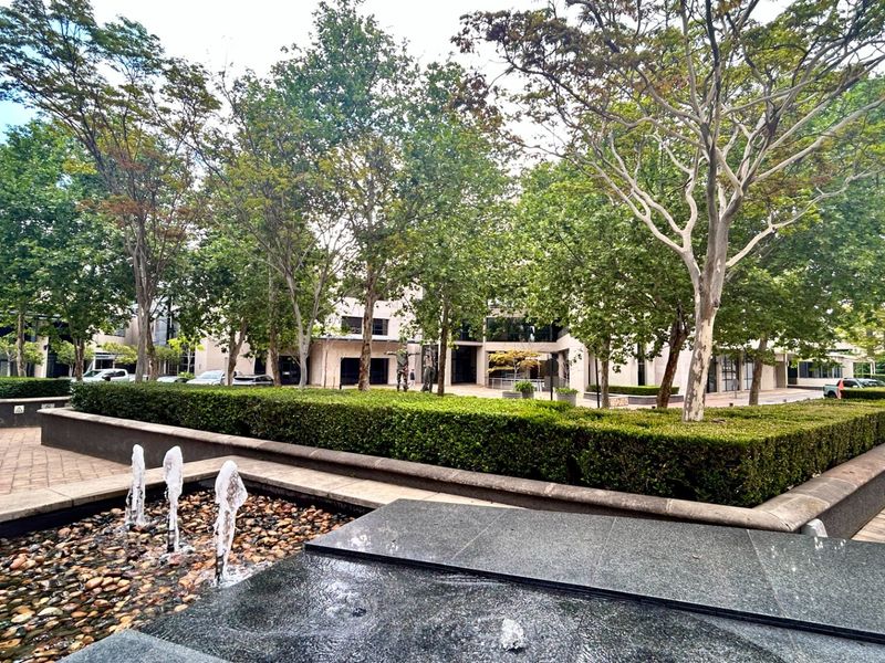 A well-maintained office courtyard featuring a central water fountain, paved walkways, and mature landscaping with manicured hedges.