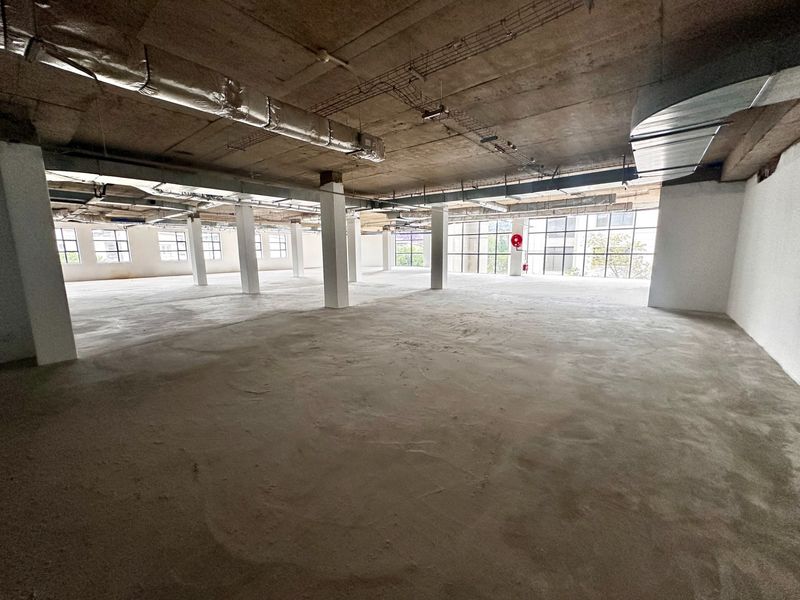 Expansive open-plan office space featuring industrial-style exposed concrete ceilings, ducting, and large windows, offering a blank canvas for custom fit-out.