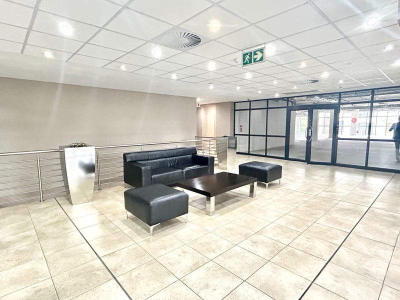 A spacious office building entrance lobby featuring tiled flooring, a suspended ceiling with recessed lighting, and modern glass partition walls.