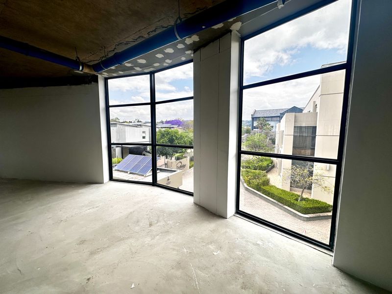An unfinished open-plan office space featuring large windows with natural light, exposed concrete ceilings, and raw flooring, ready for custom fit-out.