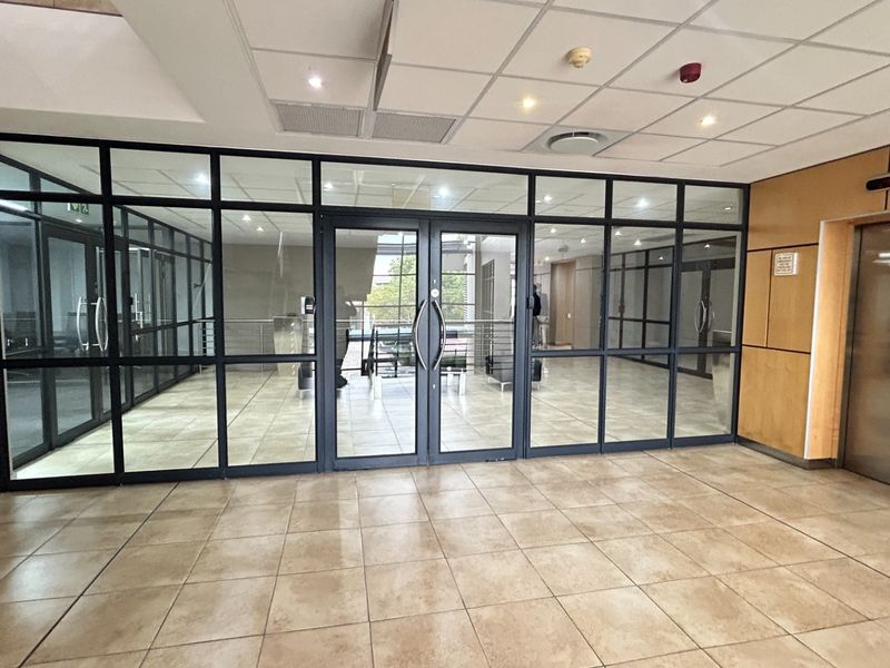 Modern office building entrance lobby featuring a glass partition wall, tiled flooring, and elevator access with wood veneer wall paneling.