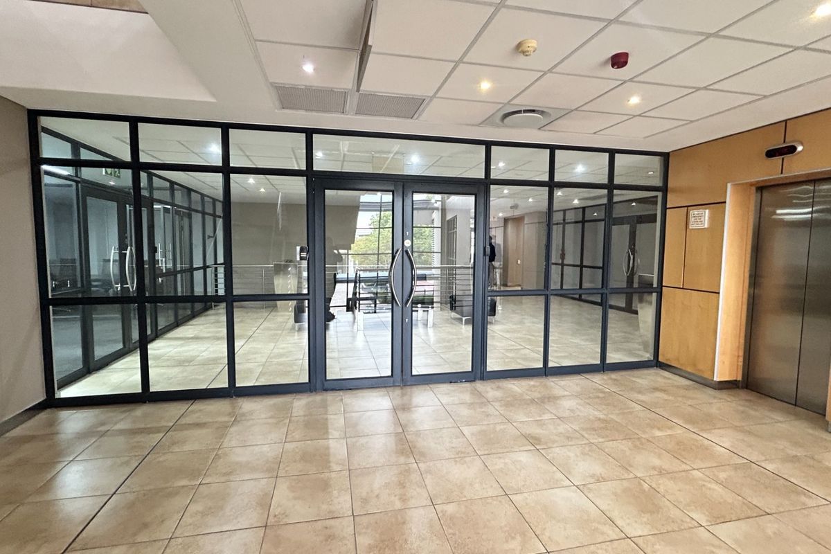 Modern office building entrance lobby featuring a glass partition wall, tiled flooring, and elevator access with wood veneer wall paneling.