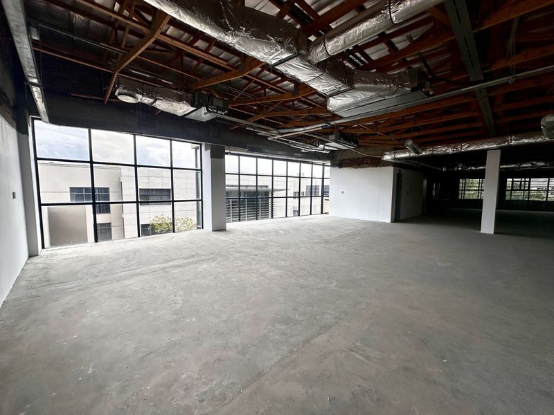 Spacious open-plan office area featuring industrial-style exposed timber trusses, HVAC ducting, and large windows providing ample natural light.