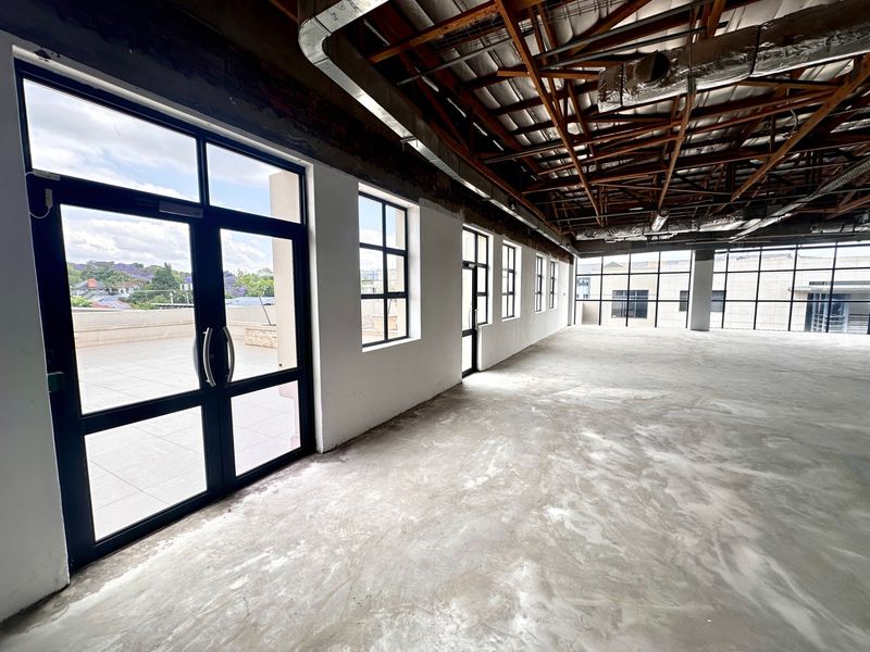 Spacious open-plan office area featuring exposed timber roof trusses, industrial HVAC ducting, concrete flooring, and large windows providing ample natural light and terrace access.