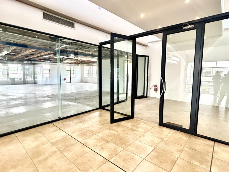 Modern open-plan office space featuring glass partitions, black aluminum framing, ceramic tile flooring, and an exposed industrial ceiling design.