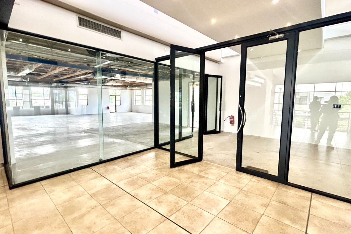 Modern open-plan office space featuring glass partitions, black aluminum framing, ceramic tile flooring, and an exposed industrial ceiling design.