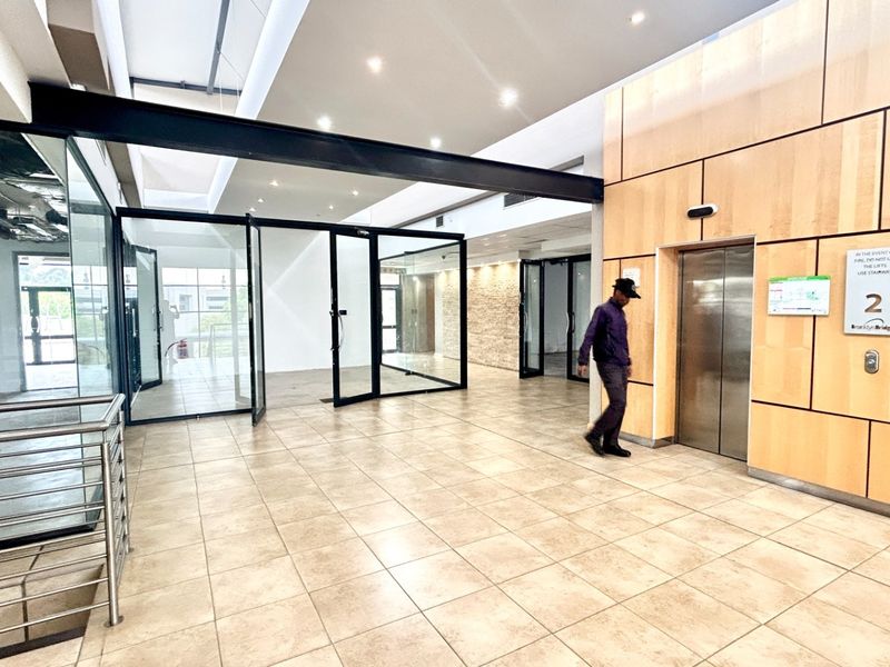 Modern office lobby area featuring tiled flooring, wood veneer wall paneling, glass partitions, and elevator access.