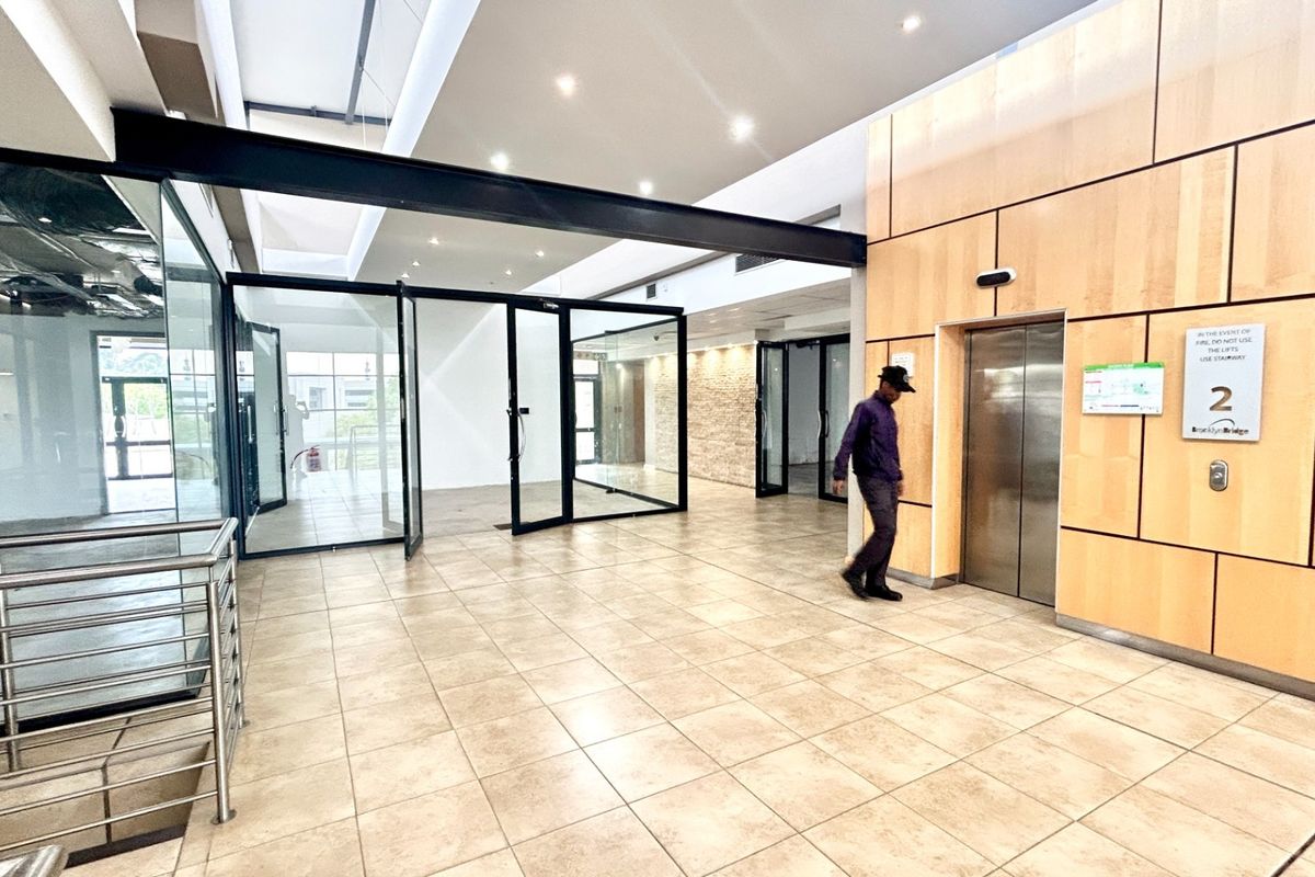 Modern office lobby area featuring tiled flooring, wood veneer wall paneling, glass partitions, and elevator access.