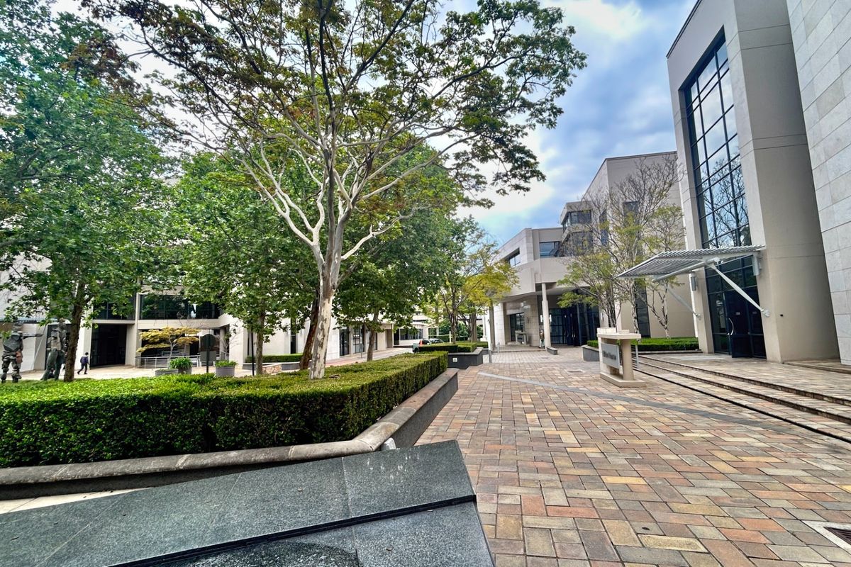 A well-maintained office courtyard featuring paved walkways, mature landscaping, and modern architectural elements including glass facades and stone cladding.