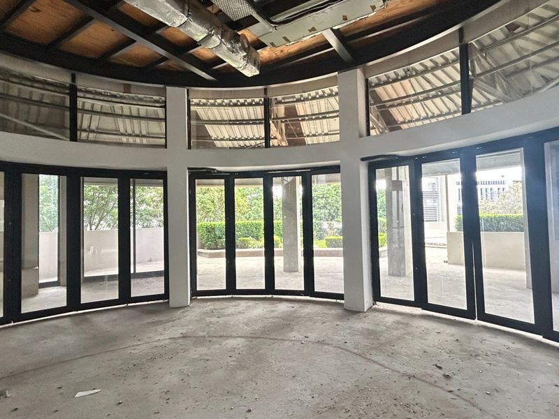 A spacious, circular office area featuring exposed ceiling structures, concrete flooring, and large bi-fold glass doors opening to an outdoor patio.