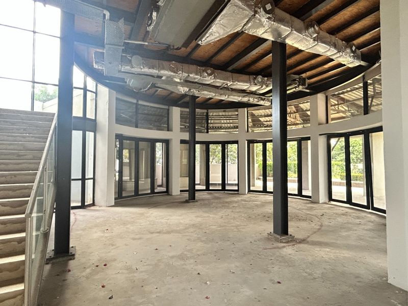 Spacious open-plan office area featuring industrial-style exposed ducting, steel columns, and floor-to-ceiling glass walls with an integrated staircase.