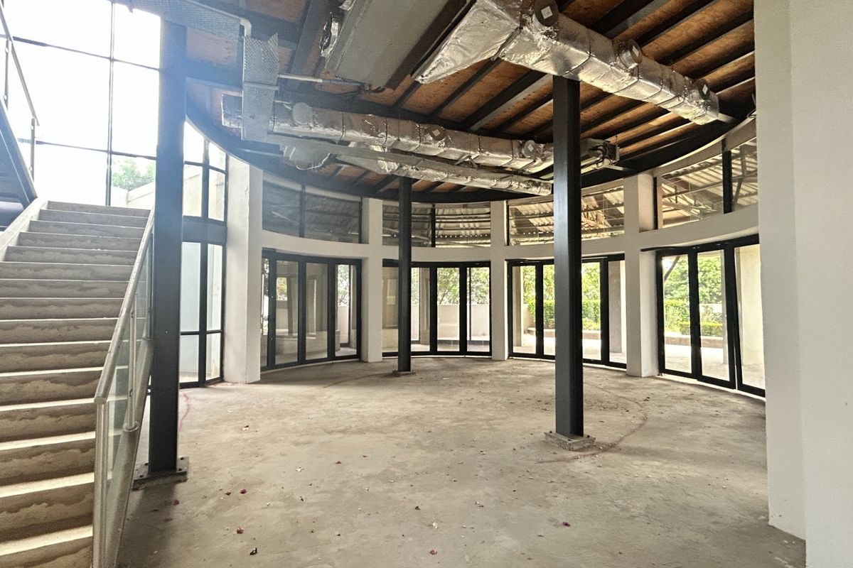 Spacious open-plan office area featuring industrial-style exposed ducting, steel columns, and floor-to-ceiling glass walls with an integrated staircase.