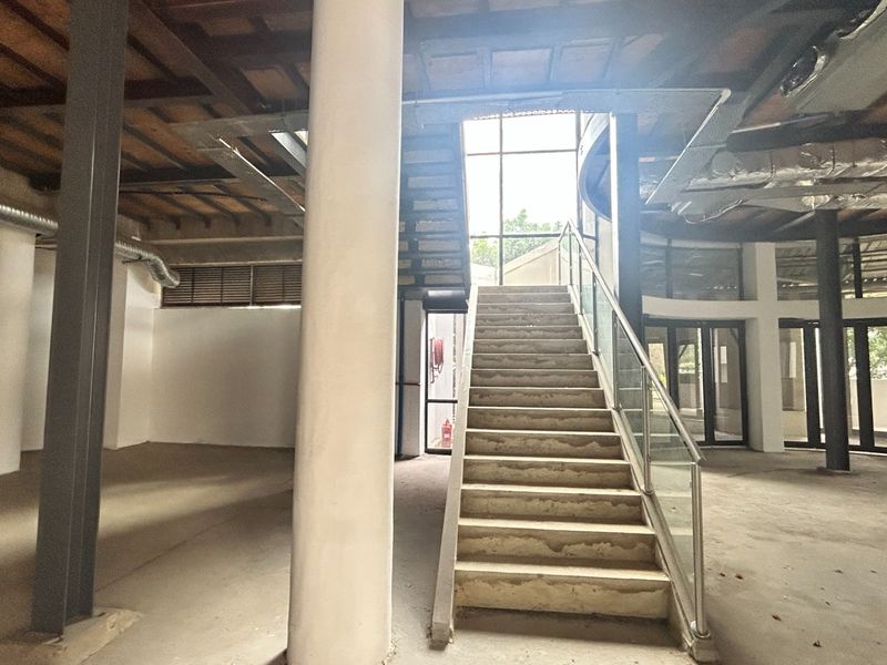 Spacious open-plan office area featuring an industrial aesthetic with exposed timber ceilings, structural columns, and a central concrete staircase with glass balustrades.