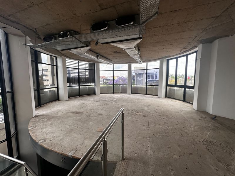 An expansive, unfinished office space featuring a curved layout, floor-to-ceiling windows with city views, and exposed industrial ceiling ductwork.