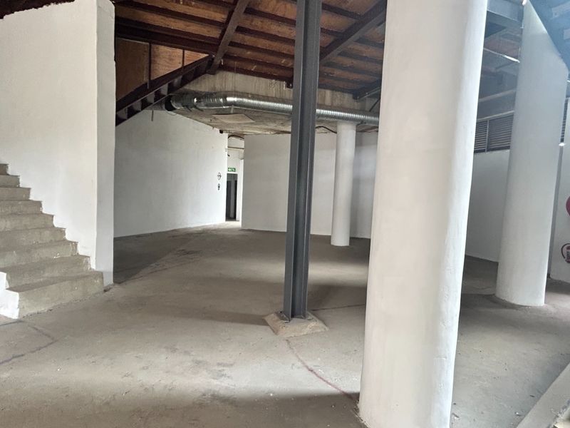 An open-plan office space featuring industrial design elements including exposed timber ceilings, steel columns, and concrete staircases, offering a versatile blank canvas.