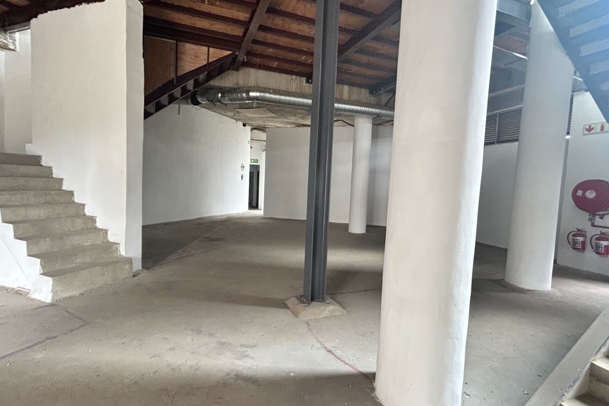 An open-plan office space featuring industrial design elements including exposed timber ceilings, steel columns, and concrete staircases, offering a versatile blank canvas.