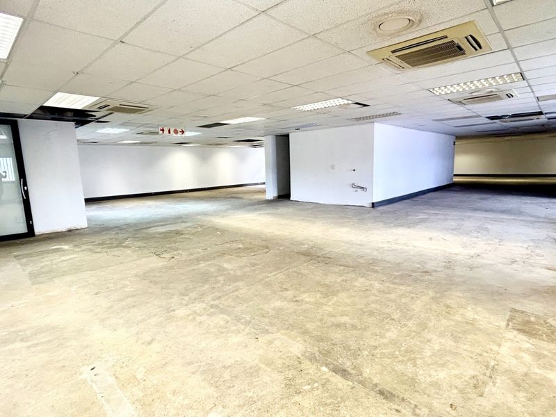 A large, open-plan office space featuring a suspended ceiling with recessed lighting, ducted air conditioning, and a glass partition door.
