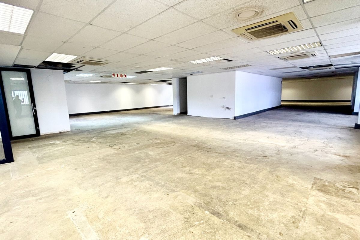 A large, open-plan office space featuring a suspended ceiling with recessed lighting, ducted air conditioning, and a glass partition door.