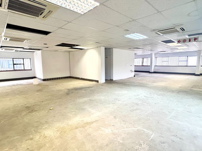 A spacious, open-plan office area featuring a suspended ceiling with integrated lighting, ducted air conditioning, and large windows with security bars.