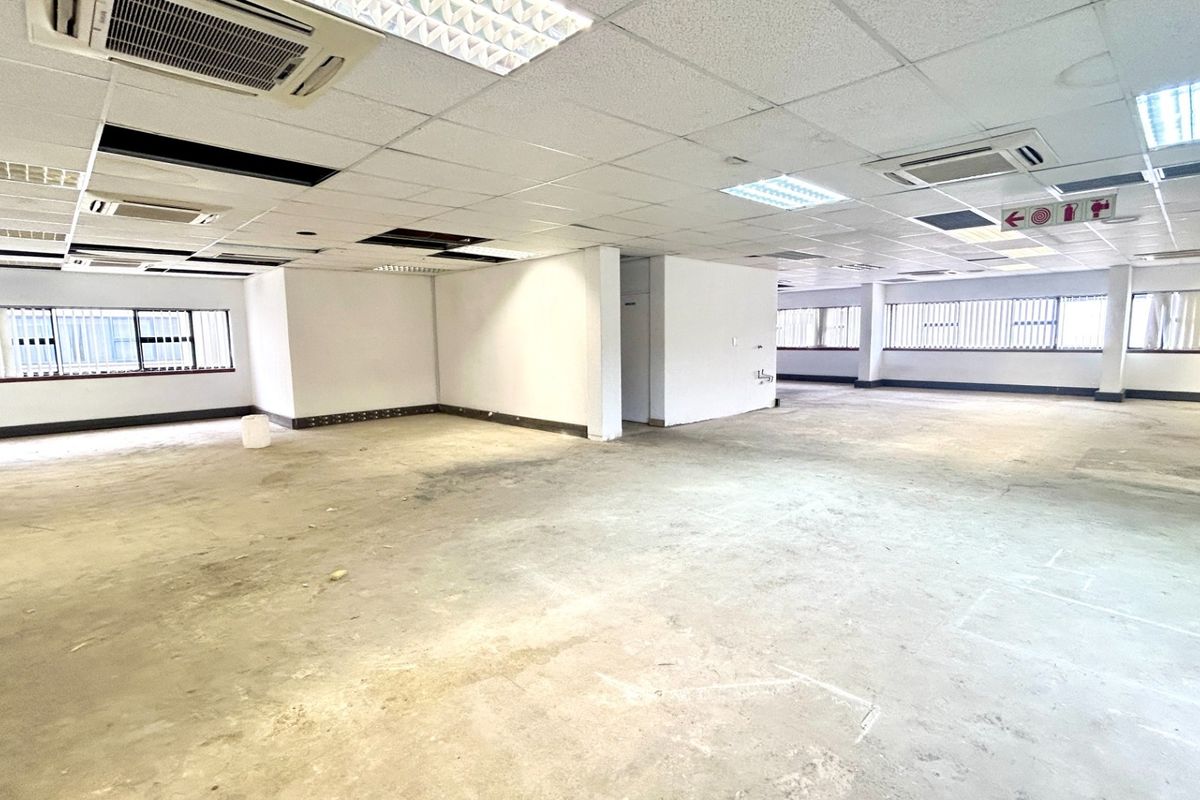 A spacious, open-plan office area featuring a suspended ceiling with integrated lighting, ducted air conditioning, and large windows with security bars.