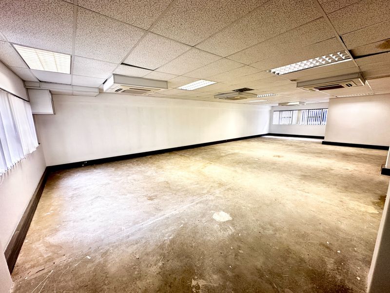 A spacious, vacant office area featuring a suspended ceiling with integrated lighting, ducted air conditioning, and large windows with vertical blinds.