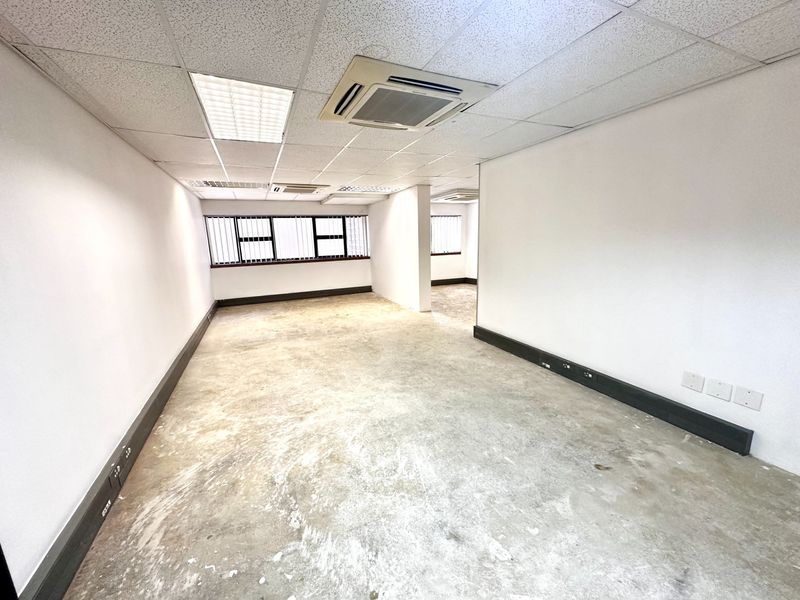 An empty, open-plan office space featuring a suspended ceiling, recessed lighting, ducted air conditioning, and power skirting along the walls.