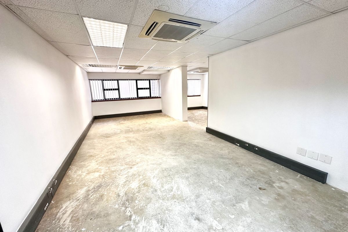 An empty, open-plan office space featuring a suspended ceiling, recessed lighting, ducted air conditioning, and power skirting along the walls.