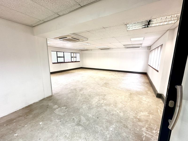 A spacious, vacant office area featuring a suspended ceiling with recessed lighting, ducted air conditioning, and large windows providing natural light.