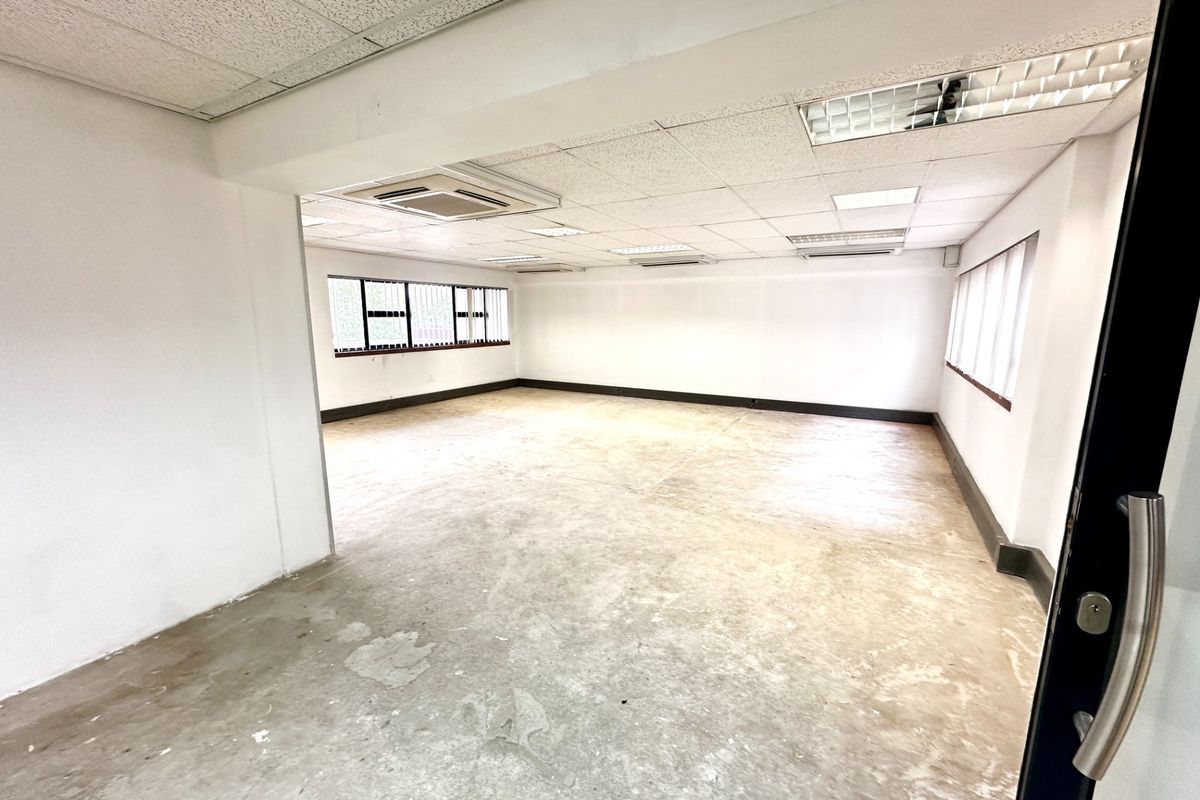 A spacious, vacant office area featuring a suspended ceiling with recessed lighting, ducted air conditioning, and large windows providing natural light.