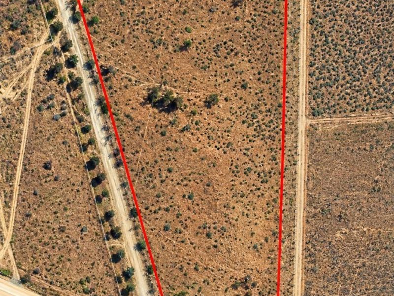 Aerial view of a vacant residential plot with natural vegetation and direct access to a dirt road.