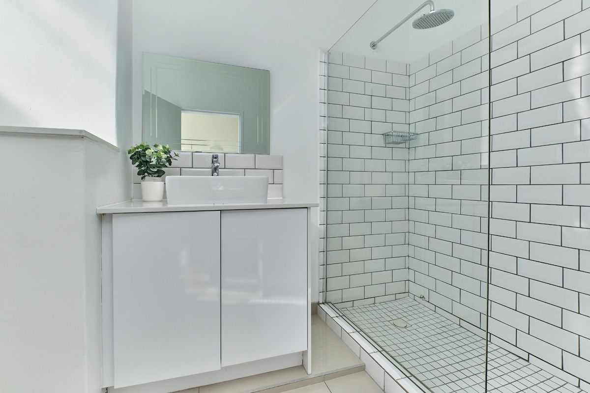 Modern bathroom featuring a white vanity with vessel sink, wall mirror, and a spacious walk-in shower with subway tile surround and glass screen.
