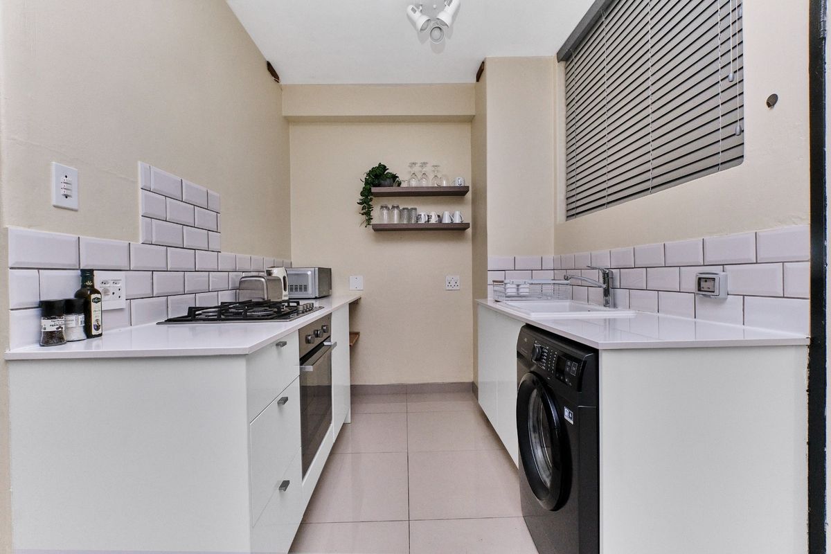 Modern galley-style kitchen featuring white cabinetry, subway tile backsplash, gas hob, built-in oven, and integrated laundry plumbing.