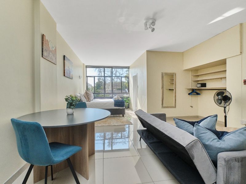 Open-plan living and bedroom area featuring polished tiled flooring, built-in shelving, and large windows providing natural light.