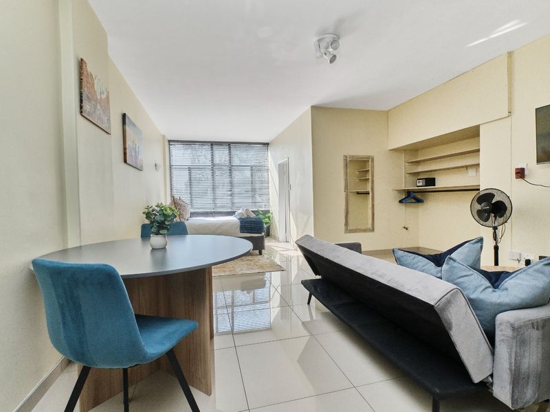 Open-plan living and sleeping area featuring polished tiled flooring, built-in shelving units, and large windows with venetian blinds.