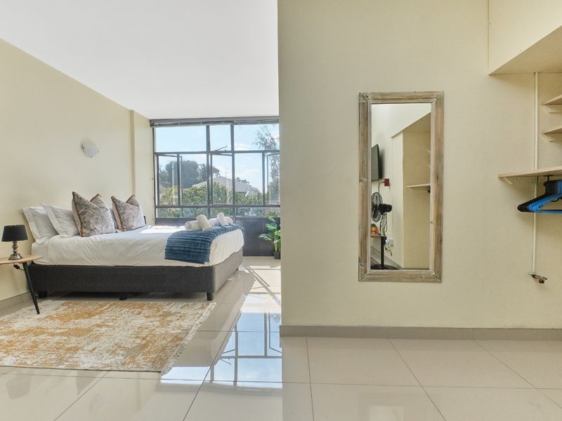 A bright bedroom featuring large windows, tiled flooring, and built-in shelving, offering a clean and functional living space.