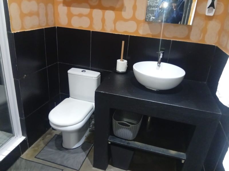 A compact bathroom featuring a white toilet, a vessel sink on a black built-in vanity, and dark wall tiling with orange painted upper walls.