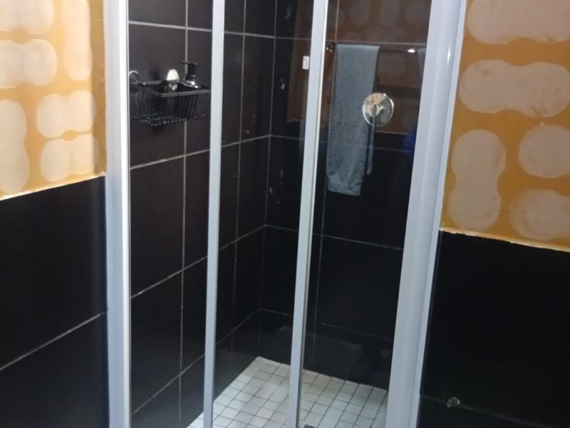 A shower enclosure featuring black wall tiles and white floor tiles, currently requiring wall finishing and painting to complete the bathroom renovation.