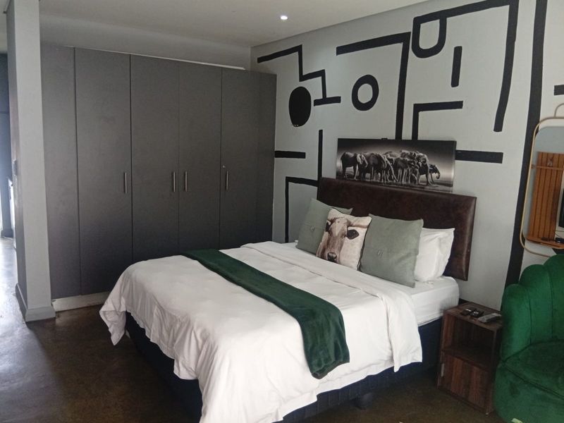 A bedroom featuring built-in cupboards and recessed downlighting, with a decorative painted feature wall.