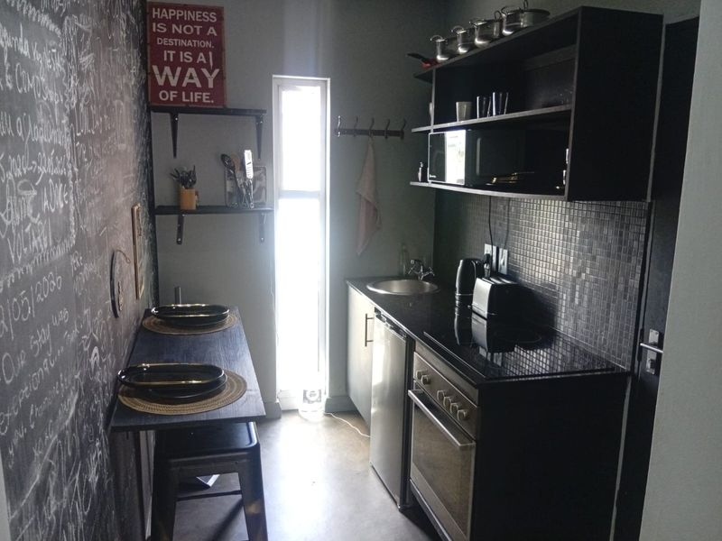 Compact kitchen featuring built-in cabinetry, an integrated oven and hob, mosaic tile backsplash, and a functional sink area.