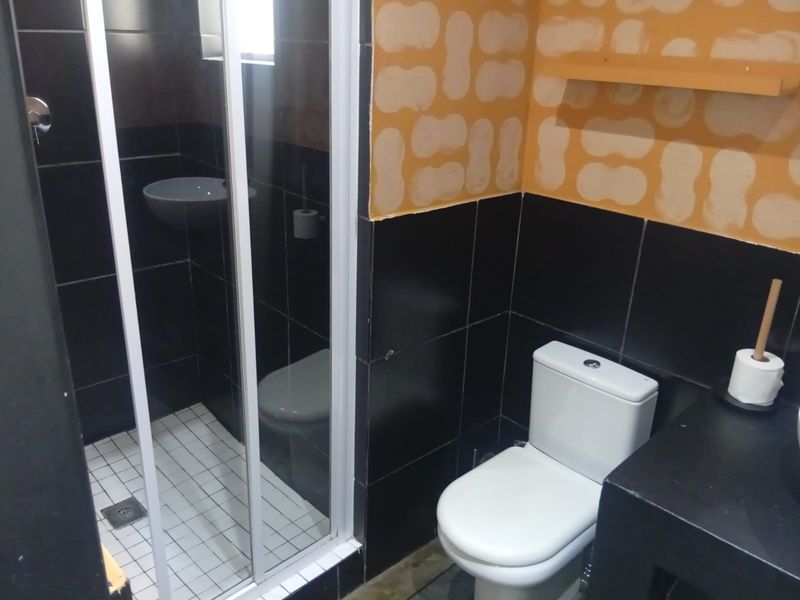 A compact bathroom featuring a shower enclosure and toilet, currently requiring wall finishing and cosmetic updates to complete the space.