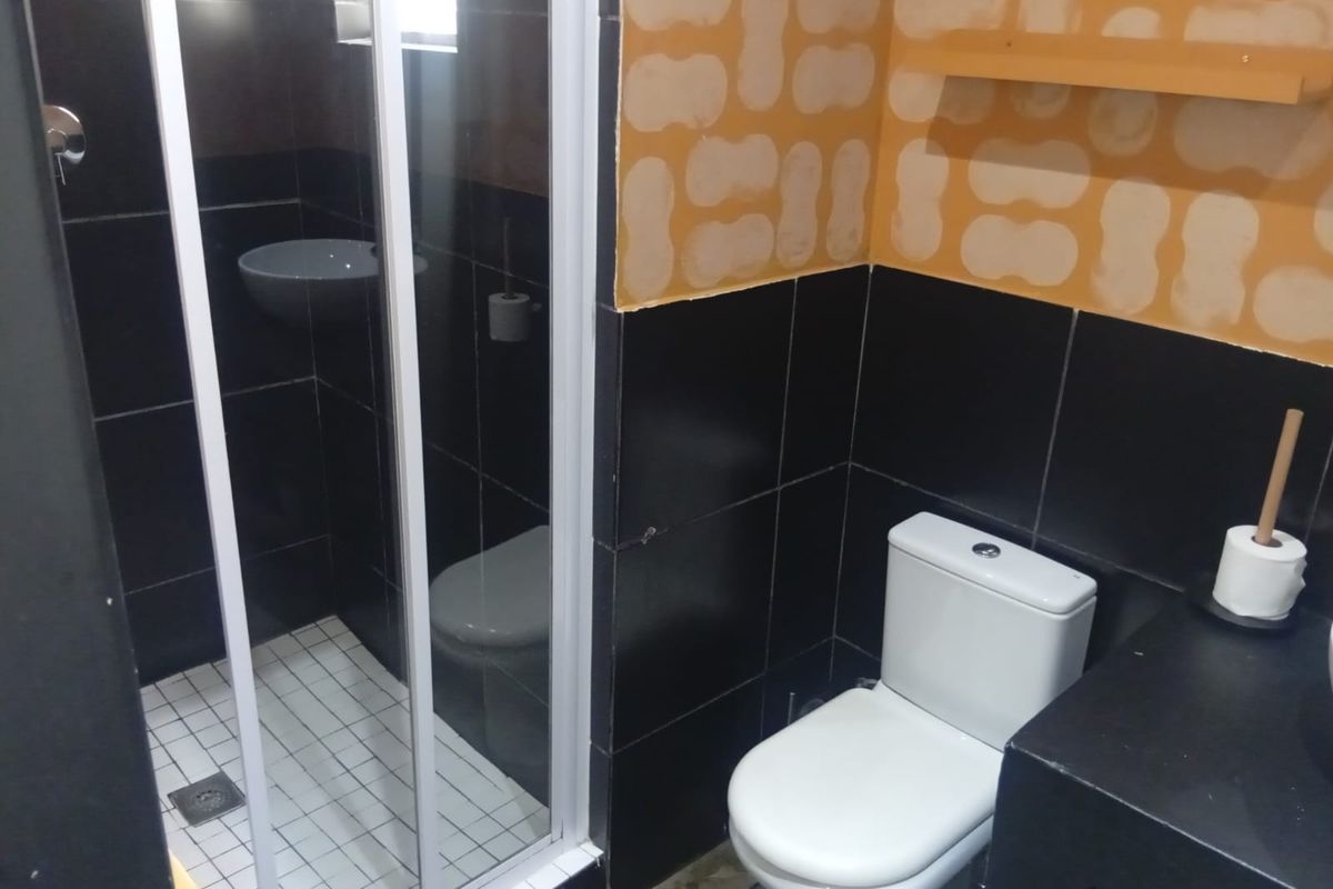 A compact bathroom featuring a shower enclosure and toilet, currently requiring wall finishing and cosmetic updates to complete the space.