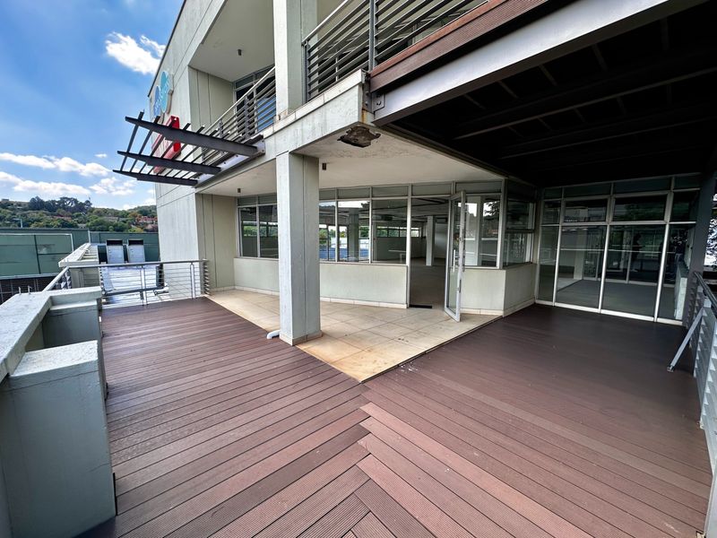 Spacious outdoor balcony featuring composite decking, tiled sections, and modern glass office frontage, offering a versatile exterior workspace or break area.