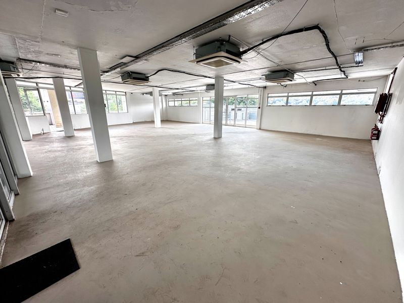 Spacious open-plan office area featuring exposed ceilings, cassette air conditioning, structural columns, and large windows providing ample natural light.